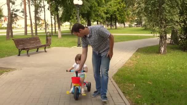 Pappa leker med sitt barn utomhus. barn lär sig cykla. begreppet lycklig familj och barndom. Föräldrar och dotter går i parken. Lycklig far lär lilla dottern att cykla. — Stockvideo