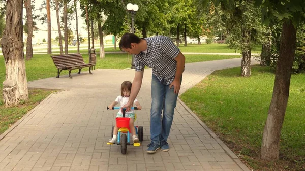 O pai brinca com o filho ao ar livre. criança aprende a andar de bicicleta. conceito de família feliz e infância. pais e filhinha caminha no parque. Pai feliz ensina a filha a andar de bicicleta . — Fotografia de Stock