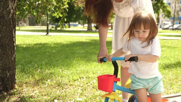 Enfant apprend à faire du vélo. concept de famille heureuse et d'enfance. parents et petite fille se promènent dans le parc. Bonne maman apprend à la petite fille à faire du vélo. mère joue avec l'enfant à l'extérieur . — Photo