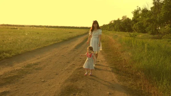 Mor och barn vilar i parken. begreppet lycklig barndom. Lilla dottern och mamma går längs vägen förbi åkern. Barnet leker rymma från mamma. lycklig familj med ett barn promenader på landsbygden. — Stockfoto