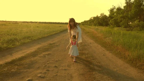 Maman et bébé se reposent dans le parc. concept d'une enfance heureuse. petite fille et maman marchent le long de la route devant le champ. enfant joue à fuir maman. famille heureuse avec un enfant marche dans la campagne . — Photo