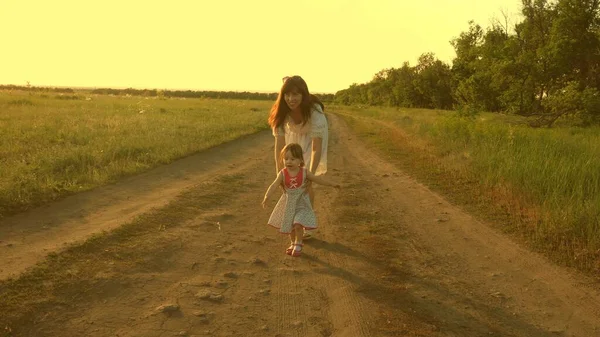 Maman et bébé se reposent dans le parc. concept d'une enfance heureuse. petite fille et maman marchent le long de la route devant le champ. enfant joue à fuir maman. famille heureuse avec un enfant marche dans la campagne . — Photo