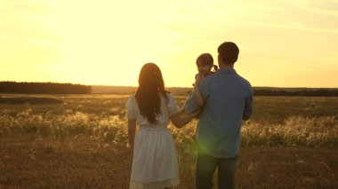 Anne ve baba, sevgili kızlarıyla birlikte gün batımında parkta yürüyorlar. Mutlu çocuk tarlada anne ve babasıyla oynuyor. Aile ve Çocukluk Konsepti