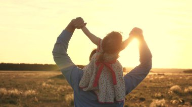 Babası sevgili kızı omuzlarında uçarken dans ediyor ve gülüyor. Mutlu çocuk gün batımı sahasında babasıyla oynuyor. Bir adam ve bir çocuğun silueti. Aile ve Çocukluk Konsepti