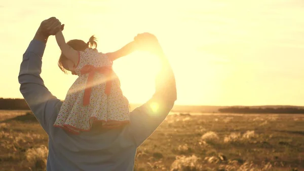 Apa a szeretett lányával a vállán táncol és nevet. Boldog gyermek játszik az apjával a naplemente mezőn. Egy férfi és egy gyerek sziluettje. Családi és gyermekkori koncepció — Stock Fotó