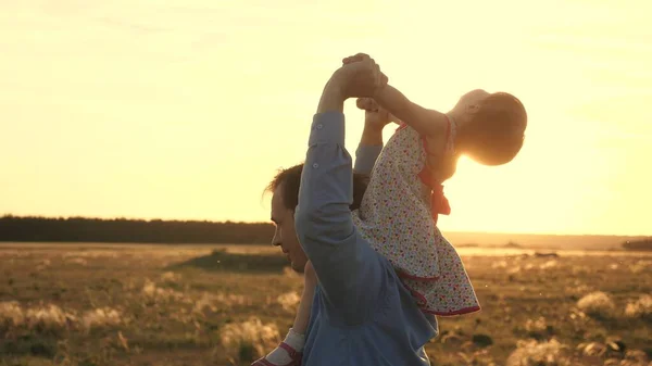 Papà con la sua amata figlia sulle spalle balla in volo e ride. Bambino felice gioca con suo padre su un campo al tramonto. La silhouette di un uomo e di un bambino. Concetto Famiglia e Infanzia — Foto Stock