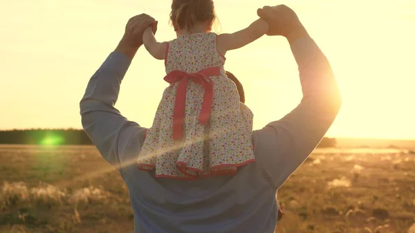 Dad with his beloved daughter on his shoulders dances in flight and laughs. Happy child plays with his father on a sunset field. Silhouette of a man and a child. Family and Childhood Concept