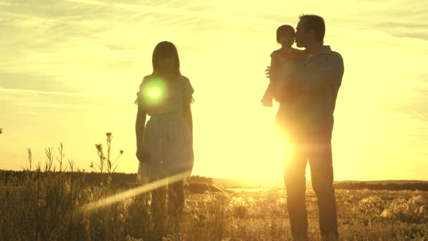 Criança feliz brinca com pai e mãe no campo. O conceito de família e filhos. Pai e mãe com sua filha amada em seus braços estão andando no parque ao pôr do sol . — Vídeo de Stock