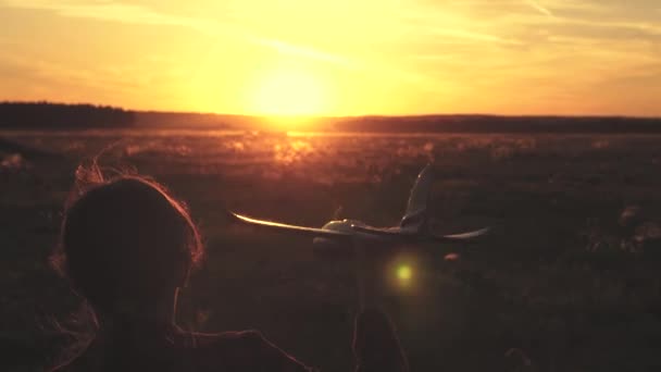 Chica feliz corre con un avión de juguete en un campo en la luz del atardecer. niños juegan juguete avión. adolescente sueña con volar y convertirse en piloto. la chica quiere convertirse en piloto y astronauta. Movimiento lento — Vídeos de Stock