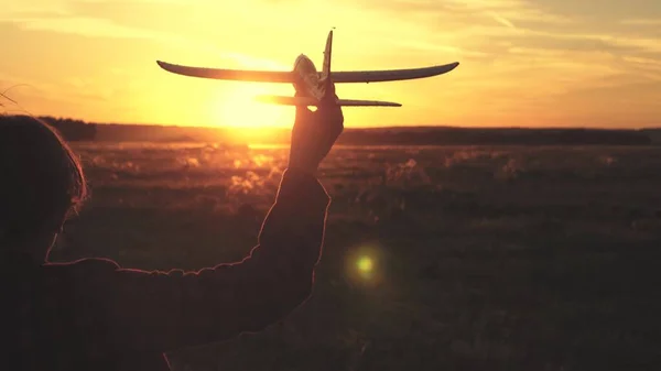 Chica feliz corre con un avión de juguete en un campo en la luz del atardecer. niños juegan juguete avión. adolescente sueña con volar y convertirse en piloto. la chica quiere convertirse en piloto y astronauta. Movimiento lento — Foto de Stock