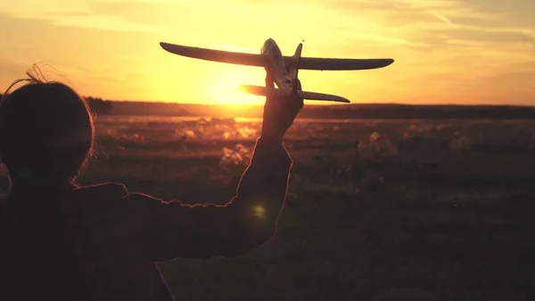 Lycklig flicka springer med ett leksaksplan på ett fält i solnedgångens sken. Barn leker leksaksflygplan. Tonåringen drömmer om att flyga och bli pilot. Flickan vill bli pilot och astronaut. Långsamma rörelser — Stockfoto