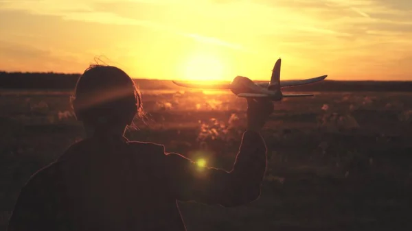 Ragazza felice corre con un aeroplano giocattolo su un campo alla luce del tramonto. i bambini giocano aereo giocattolo. adolescente sogna di volare e diventare pilota. la ragazza vuole diventare pilota e astronauta. Rallentatore — Foto Stock