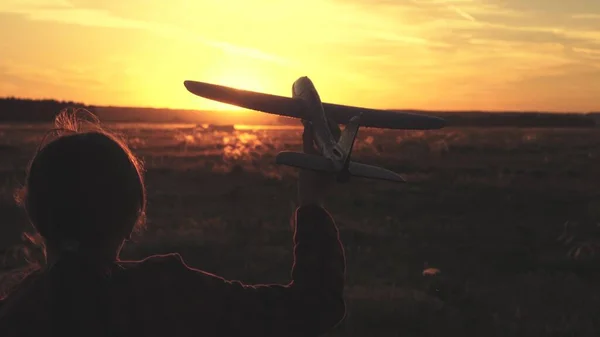 Menina feliz corre com um avião de brinquedo em um campo sob a luz do pôr do sol. As crianças brincam de avião de brinquedo. sonho adolescente de voar e se tornar piloto. a menina quer se tornar piloto e astronauta. Movimento lento — Fotografia de Stock