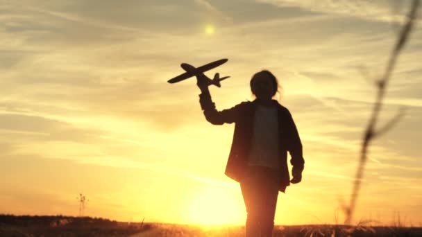 Ragazza felice corre con un aeroplano giocattolo su un campo alla luce del tramonto. i bambini giocano aereo giocattolo. adolescente sogna di volare e diventare pilota. la ragazza vuole diventare pilota e astronauta. Rallentatore — Video Stock