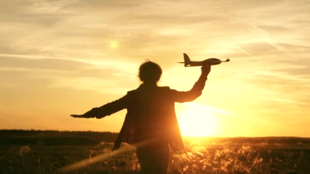 Chica feliz corre con un avión de juguete en un campo en la luz del atardecer. niños juegan juguete avión. adolescente sueña con volar y convertirse en piloto. la chica quiere convertirse en piloto y astronauta. Movimiento lento — Vídeo de stock