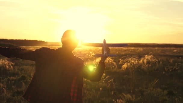 Lycklig flicka springer med ett leksaksplan på ett fält i solnedgångens sken. Barn leker leksaksflygplan. Tonåringen drömmer om att flyga och bli pilot. Flickan vill bli pilot och astronaut. Långsamma rörelser — Stockvideo