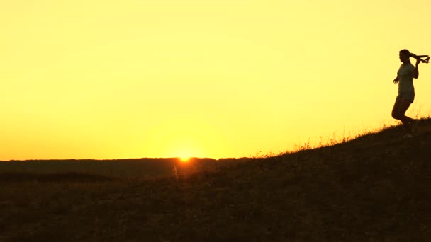 Dreams of flying. Silhouette of children playing on plane. Children run from the mountain with an airplane in hand at sunset. Happy childhood concept. girls play with a toy plane at sunset. — ストック動画