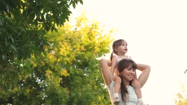 Conceito de infância feliz. mãe carrega em seus ombros seu filho amado, no parque. A mãe caminha com a filha nos ombros debaixo das árvores. Família feliz está relaxando no parque . — Vídeo de Stock