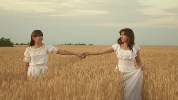 Young mother and daughter are holding hands running along a golden wheat field. slow motion. happy family travels field, hand in hand. concept of a happy family. beautiful mom and adult daughter. — Stok video