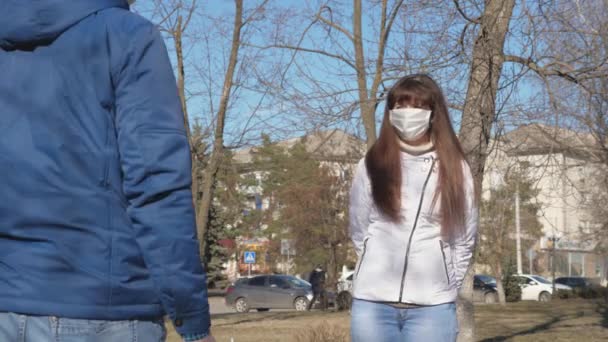 Коронавирус. Молодая девушка в защитной маске и мужчина в защитной маске встречаются на улице. Пандемия коронавируса. туристы на улицах носят защитную маску от вирусов. концепция здоровья и безопасности, N1H1 — стоковое видео