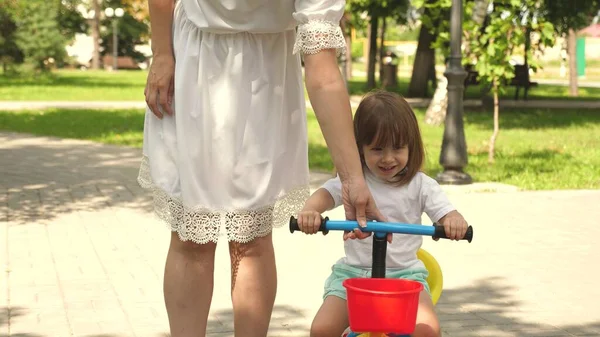 Šťastná máma učí malou dceru jezdit na kole. Matka si venku hraje s dítětem. dítě se naučí jezdit na kole. koncept šťastné rodiny a dětství. rodiče a malá dcera procházky v parku. — Stock fotografie