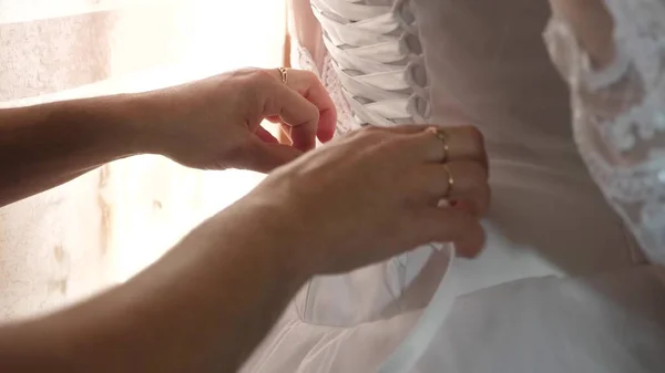 The bride dresses a white wedding dress. Bridesmaids tie the ribbons in the back of the brides dress. girl dresses a beautiful dress. — Stockfoto