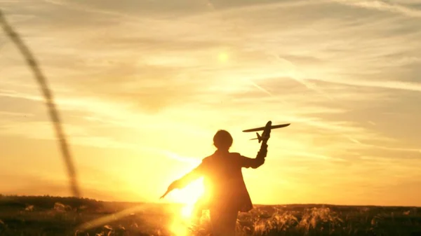 Chica quiere convertirse en piloto y astronauta. En cámara lenta. Chica feliz corre con un avión de juguete en un campo en la luz del atardecer. niños juegan juguete avión. adolescentes sueña con volar y convertirse en piloto. — Foto de Stock