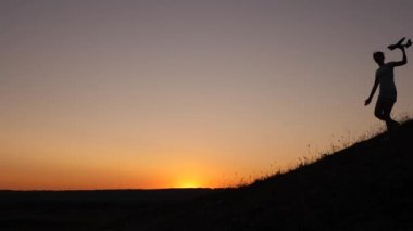 Kızlar gün batımında oyuncak uçakla oynarlar. Uçakta oynayan çocukların silueti. Uçma hayalleri. Mutlu çocukluk kavramı. Çocuklar ellerinde bir uçakla dağdan kaçarlar..
