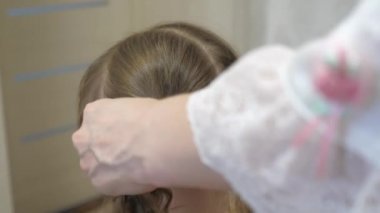 Mutlu bir aile. Kız için güzel saç stili kavramı. Anne, çocuğun saçlarını bir tarakla tarıyor. Anne, küçük kızının saçını örüyor..