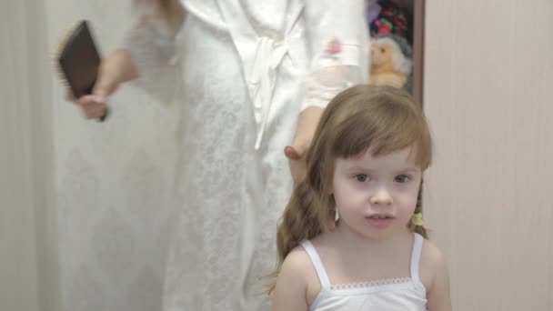 Mother combs the childs hair with a comb. concept of beautiful hairstyle for daughter. a happy family. Mom Braids the Braid Of Her Little Daughter. — Stock Video