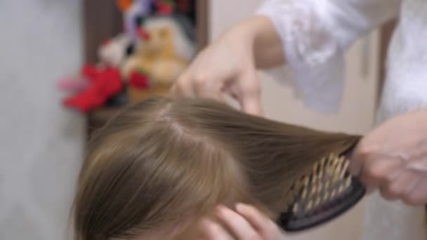 Concept de belle coiffure pour fille. une famille heureuse. Maman tresse la tresse de sa petite fille. mère peigne les cheveux des enfants avec un peigne . — Video