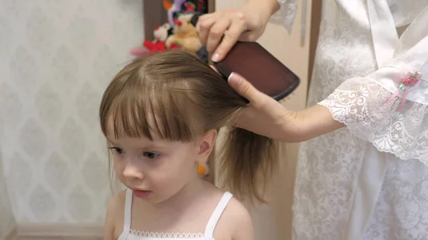 Η μητέρα χτενίζει τα μαλλιά του παιδιού με μια χτένα. έννοια του όμορφου hairstyle για την κόρη. μια ευτυχισμένη οικογένεια. Η μαμά πλέκει την κόρη της. — Φωτογραφία Αρχείου