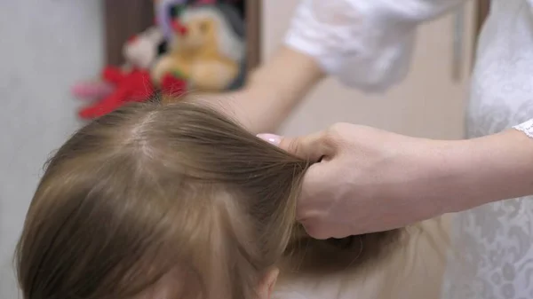 Έννοια του όμορφου hairstyle για την κόρη. μια ευτυχισμένη οικογένεια. Η μαμά πλέκει το στήθος της κόρης της. Η μητέρα χτενίζει τα μαλλιά του παιδιού με χτένα.. — Φωτογραφία Αρχείου