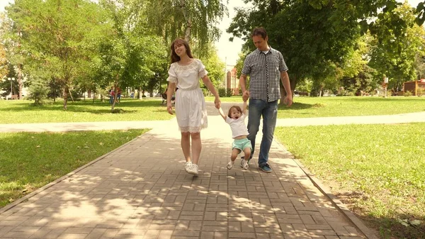 Gelukkig kind speelt met papa en mama houdt hun hand vast en springt. Kleine dochter springt hand in hand met papa en mama in het park. Familie concept. Wandelen met een klein kind in de natuur. — Stockfoto