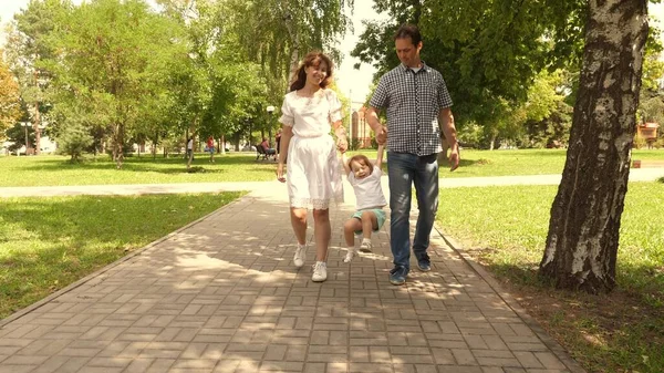 Gelukkig kind speelt met papa en mama houdt hun hand vast en springt. Kleine dochter springt hand in hand met papa en mama in het park. Familie concept. Wandelen met een klein kind in de natuur. — Stockfoto