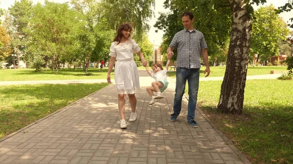 Glada barn leker med pappa och mamma håller sina händer och hoppar. Lilla dottern hoppar i hand med pappa och mamma i parken. Familjebegreppet. Promenader med små barn i naturen. — Stockfoto