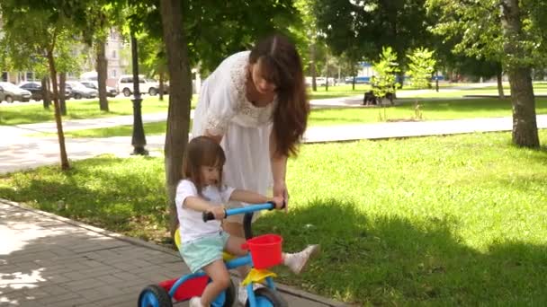 Concept of happy family and childhood. child learns to ride bicycle. parents and little daughter walks in park. Happy mom teaches little daughter to ride a bike. mother is playing with child outdoors. — Stock Video