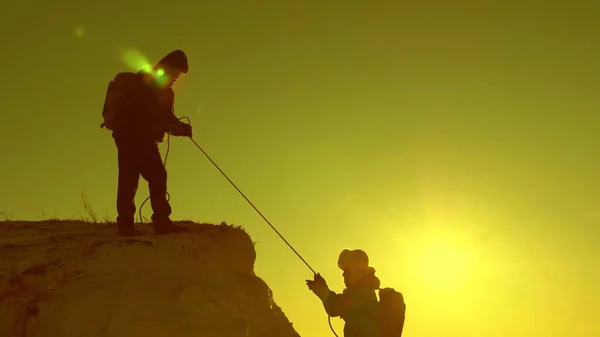 Альпіністи піднімаються на мотузці. Дівчата-мандрівники ламаються і падають зі скелі. командна робота туристів. подорожувати в горах на заході сонця. бізнесмени страхують один одного. допомога в складних умовах . — стокове фото