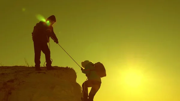 Scalatori scalano la montagna su una corda. Una viaggiatrice crolla e cade da una scogliera. lavoro di squadra di turisti. viaggiare in montagna al tramonto. Gli uomini d'affari si assicurano a vicenda. aiuto in circostanze difficili . — Foto Stock