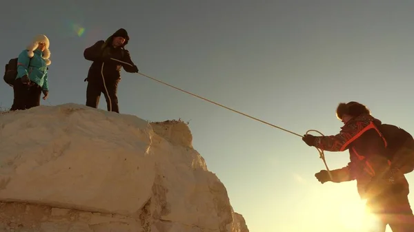 Команда альпинистов взбирается на гору по веревке. свободная женщина помогает мужчине подняться на гору. Командная работа туристов. Путешествие и приключения в горах на закате. бизнесмены страхуют друг друга . — стоковое фото