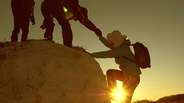 Team di scalatori sale una montagna tendendo una mano l'uno all'altro. Donna libera viaggiatore scalare la montagna. lavoro di squadra di turisti. Viaggio e avventura in montagna al tramonto . — Foto Stock