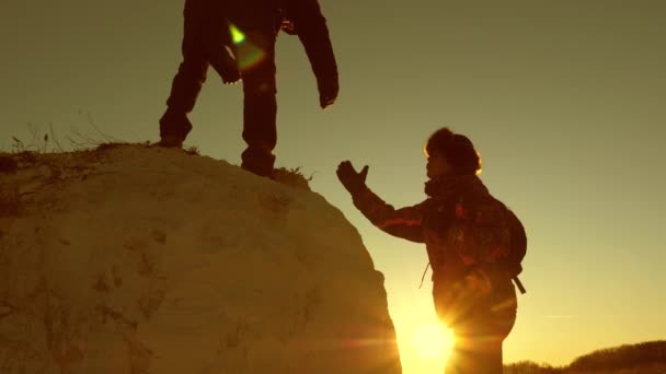hegymászók csapata felmászik egy hegyre, segítő kezet nyújtva egymásnak. Szabad nő utazó mászni hegyet. Turisták csapatmunkája. Utazás és kaland a hegyekben naplementekor.