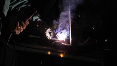 Parlak ışık ve kaynaktan çıkan kıvılcımlar. Metal işleme tesisinde endüstriyel üretim yapan metal yapıları kaynak yapmak için modern kaynak makinesi kullanan koruyucu bir maske takan endüstriyel işçiler..