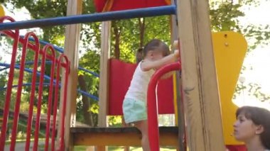 Anne ve bebek parkta oynuyorlar. Mutlu çocukluk kavramı. Mutlu çocukluk ve aile kavramı. Küçük çocuk gülüyor ve parktaki oyun alanının tadını çıkarıyor. Çocuk sokakta annesiyle oynuyor..
