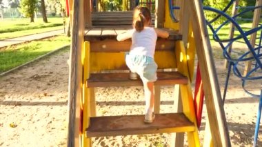 Çocuk merdivenlerden çıkıp çocuklar kayıyor. Anne ve bebek oyun bahçesinde oynuyorlar. Mutlu çocukluk kavramı. Mutlu çocukluk ve aile kavramı. Küçük çocuk gülüyor ve parkta oyun oynamaktan hoşlanıyor.