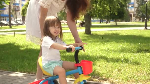 A mãe feliz ensina a filha a andar de bicicleta. mãe está brincando com a criança ao ar livre. conceito de família feliz e infância. criança aprende a andar de bicicleta. pais e filhinha caminha no parque . — Vídeo de Stock
