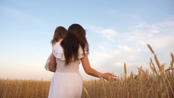 Concepto familiar feliz. madre camina con un niño en un campo con trigo. mamá y su hijita están jugando en un campo de trigo maduro al sol. familia feliz viaja. bebé en los brazos de mamá . — Vídeo de stock