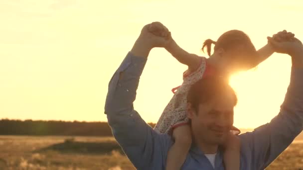 Pappa med sin älskade dotter på axlarna dansar på flykt och skrattar. Glada barn leker med sin far på ett solnedgångs fält. Silhuett av en man och ett barn. Familje- och barndomsbegreppet — Stockvideo