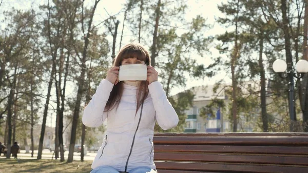 Una joven con una máscara protectora en la calle. Coronavirus pandémico. mujer turista en un parque en un banco lleva una máscara protectora de los virus. concepto salud y seguridad, coronavirus N1H1, protección contra virus . —  Fotos de Stock