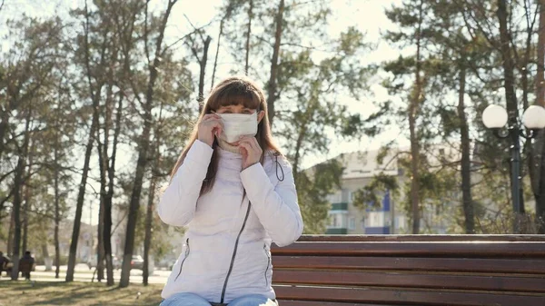 Een jong meisje met een beschermend masker op straat. Pandemisch Coronavirus. vrouw toerist in een park op een bank draagt een beschermend masker tegen virussen. concept gezondheid en veiligheid, N1H1 coronavirus, virusbescherming. — Stockfoto